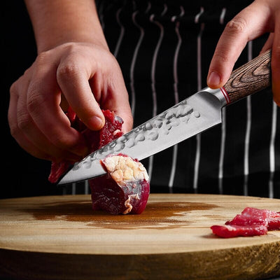 Personne en train de couper morceau de viande avec un couteau de cuisine avec un manche en bois sur une planche à découper en bois.