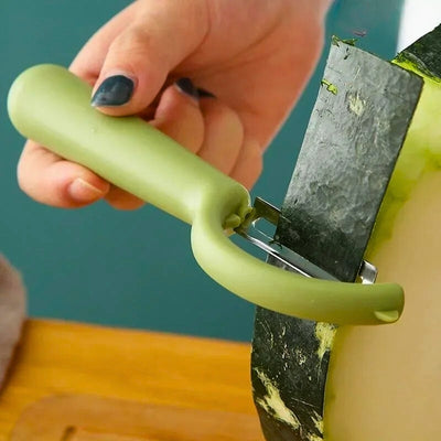 Personne en train d'éplucher une aubergine avec un économe vers au-dessus d'une table, l'épluchure passe dans la lame de l'appareil.