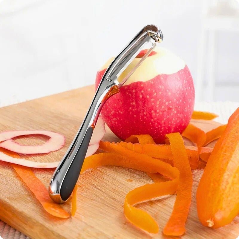 Epluche légumes posé à cheval sur une pomme et une planche en bois.