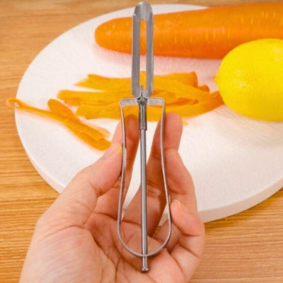 Éplucheur présenté dans la main gauche d'une personne, en arrière-plan une assiette de légumes.