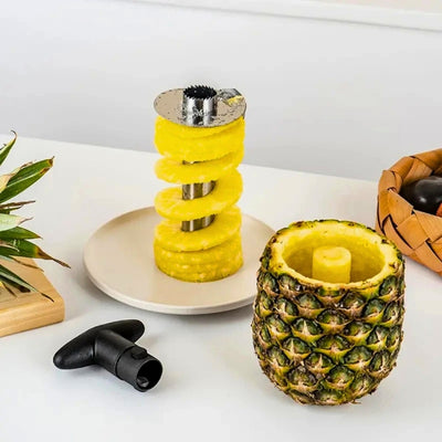 Éplucheur posé dans une assiette à la verticale avec de l'ananas dessus, à côté la coque e l'ananas vide et la poignée de l'appareil.