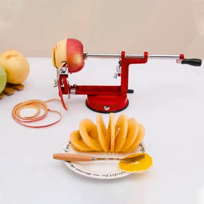 Éplucheur pomme posé sur une table avec une pomme en train de se faire éplucher et couper, les épluchures courent sur la table, à côté des fruits posé sur un repose plat, et en premier plan une pomme déjà épluchée et coupée dans une assiette.