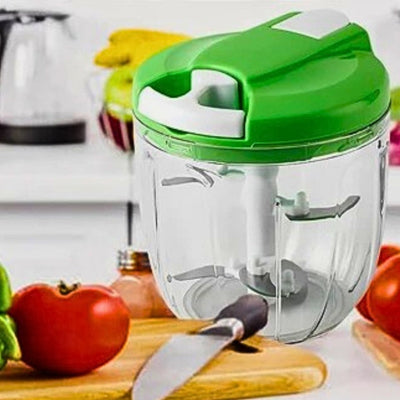 Hachoir manuel vert à côté d'un couteau, d'une planche à découper et d'une tomate