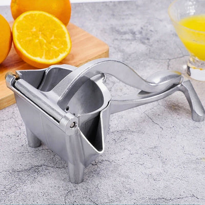 Presse agrume manuel posé sur une table devant une planche à découper qui a des oranges dont certaines coupées dessus.