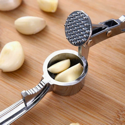 Presse ail ouvert avec des gousses d'ail à l'intérieur du réservoir, il est posé sur une planche à découper à côté de gousses d'ail.