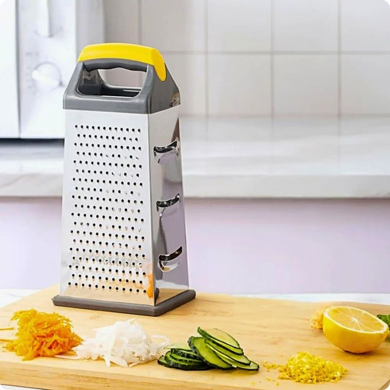 Râpe à fromage manuelle sur planche derrière des légumes râpés ou tranchés.