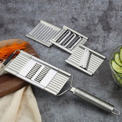râpe à légumes manuelle inox interchangeal'ine posée sur une table à côté des lames interchangeables.