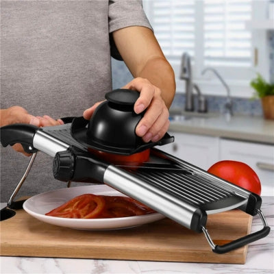 Mandoline japonaise posée sur une planche à découper et utilisée par une personne pour couper une tomate en tranche. Les tranches tombent dans une assiette positionnée dessous.