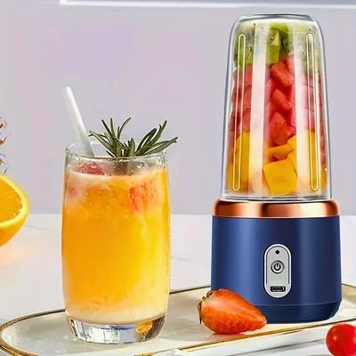 Mini blender posé sur table à côté d'un verre de jus de fruit.