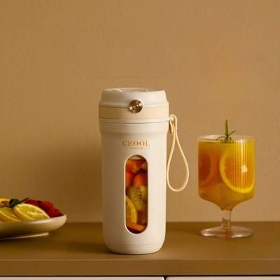 blender portable posé sur table à côté d'un verre de jus d'orange.