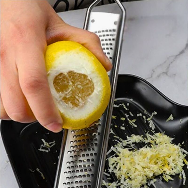 Personne qui utilise un zesteur au-dessus d'une assiette pour récupérer des zestes de citron.