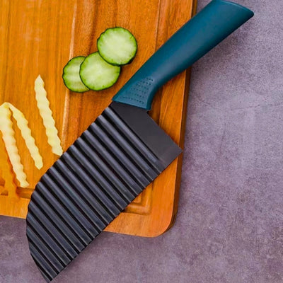 Coupe frite avec lame ondulée de couleur noire posé sur une planche à découper en bois à côté de rondelle de concombre et de pommes de terre coupés en frites