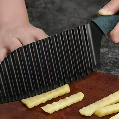 Coupe frite avec lame ondulée de couleur noire en train de couper une pomme de terre sur une planche à découper