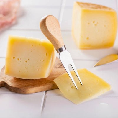 Fourchette à fromage posé sur un fromage qui est posé sur une planche à découper en bois.
