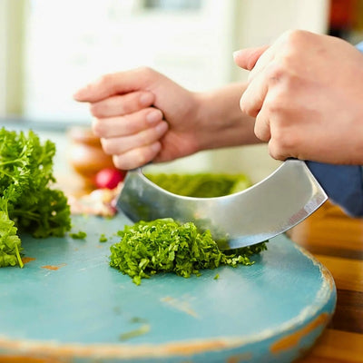 Mains qui tiennent un couteau hachoir et qui coupe de la salade sur un plan de travail de couleur bleu