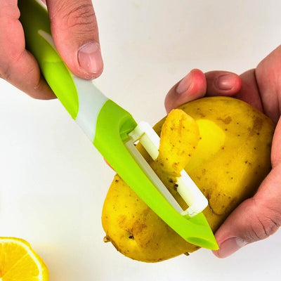 Personne en train d'éplucher une pomme de terre avec un econome dans le coin gauche une tranche de citron.