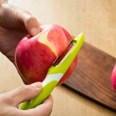 Personne en train d'éplucher une pomme avec un econome en arrière-plan une planche.