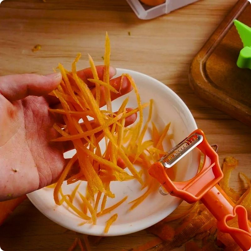 Personne tenant des carottes en julienne dans une main et un économe à julienne dans l'autre main dans une cuisine.