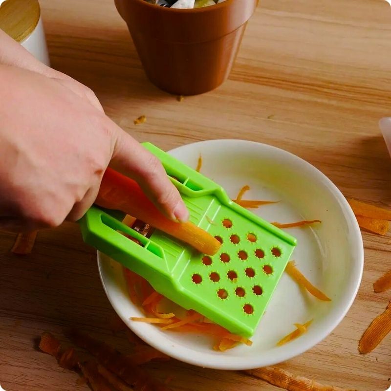 Personne râpant une carotte à l'aide d'un économe à julienne dans une cuisine et de son support prévu à cet effet.