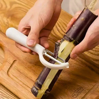 Personne en train d'éplucher un morceau de bambou avec un économe blanc au-dessus d'une planche à découper en bois, l'épluchure passe dans la lame de l'appareil.