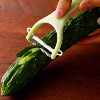 Personne en train d'éplucher un concombre avec un économe de couleur vert. On voit une épluchure passer dans la lame de l'économe.
