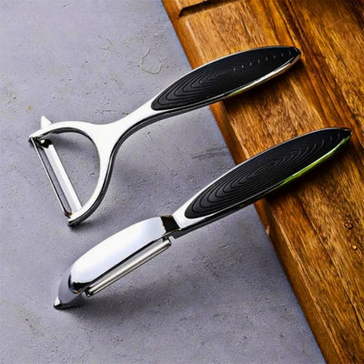 Un économe à lame horizontale et un économe à lame verticale posés à cheval sur une table et une planche à découper en bois pour être présentés.