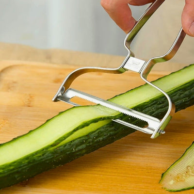Personne en train de couper en lamelle un concombre sur une planche à découper en bois, une lamelle passe dans l'économe.