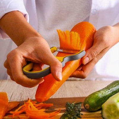 Mains d'une personne en train de couper en julienne une carotte à l'aide d'un économe de couleur orange et noire. Elle tient la carotte de la main gauche et l'économe de la main droite.