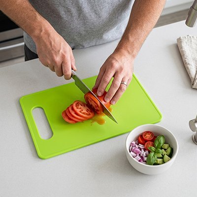 Ensemble de planches à découper colorées, homme qui utilise la planche vert pour couper des tomates