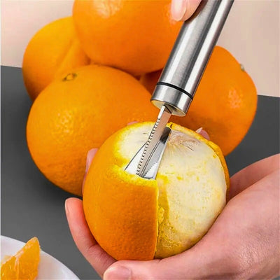 Personne en train d'éplucher une orange avec un éplucheur adapté, en utilisant l'avant de l'éplucheur, en arrière un tas d'orange.