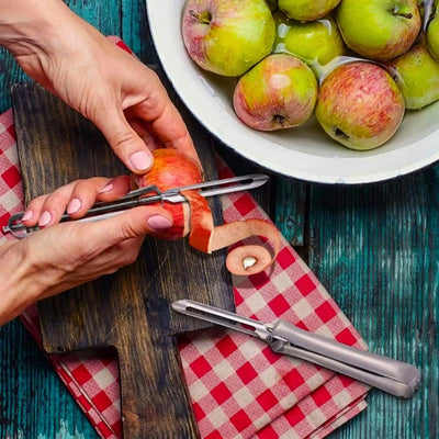 Personne en train d'éplucher une pomme au-dessus d'une planche à découper en bois et un torchon. Les épluchures court de l'éplucheur à la planche. En arrière une grande assiette remplit de pomme.