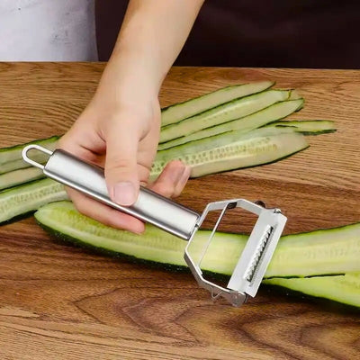 Personne en train de faire des lamelles de concombre avec un éplucheur, le concombre est posé sur une table, des épluchures sont déjà coupées.