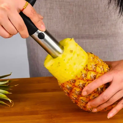 Personne en train d'éplucheur un ananas avec un éplucheur prévu à cet effet. On voit la moitié de l'ananas sortie de la peau de l'ananas avec une barre métallique.