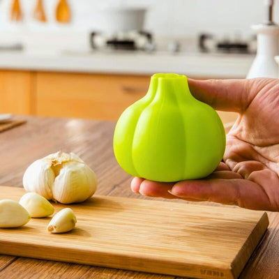 Personne qui tient dans sa main un éplucheur au-dessus d'une planche à découper en bois située dans une cuisine, sur laquelle est posé de l'ail et des gousses d'ail.