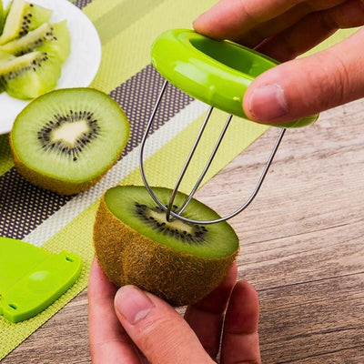 Mains d'une personne en train d'éplucher un kiwi avec un éplucheur spécialement conçu pour ce fruit. Elle est en train d'introduite la lame dans le fruit. En arrière-plan, une assiette remplit de Kiwis coupés