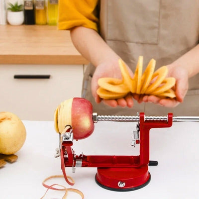 Éplucheur pomme posé sur une table avec une pomme en train de se faire éplucher et couper, en arrière-plan une personne tient une pomme déjà épluchée et coupée.
