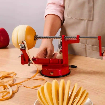 Personne en train d'éplucher une pomme à l'aide d'un éplucheur pomme, l'appareil est posé sur une table, on voit la pomme en train d'être épluchée et coupé, les épluchures courent sur la table, en premier plan une pomme déjà épluché et coupé dans une assiette.