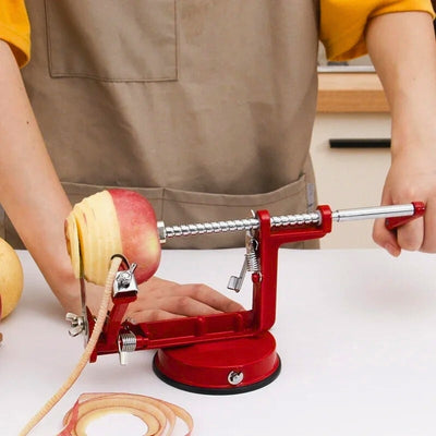 Personne en train d'éplucher une pomme à l'aide d'un éplucheur pomme, l'appareil est posé sur une table, on voit la pomme en train d'être épluchée et coupé, les épluchures courent sur la table, il tient la poignée de l'appareil avec sa main gauche.