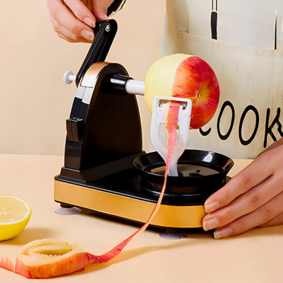 Personne en train de tourner la manivelle d'un éplucheur à pomme en le tenant de l'autre main, la peau coupée de la pomme est étalé e le long de la table avec un morceau de citron à côté.