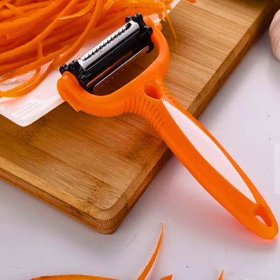 Éplucheur orange posé à cheval sur une table et une planche à découper en bois, sur la planche une assiette de carottes coupées en julienne.