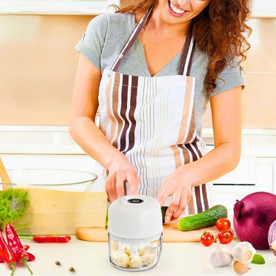 Femme en train de réaliser ses préparations de cuisine avec un hachoir electrique devant elle, sur le côté des légumes