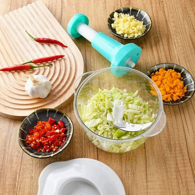 Réservoir d'un hachoir manuel remplit d'ail haché avec les lames encore dedans à côté, la tête de l'appareil et des petites assiettes d'aliments hachés.
