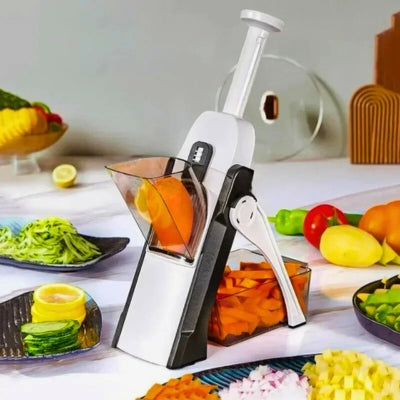 Mandoline cuisine grise posée sur une table et entourée d'assiette remplit de légumes coupés de différentes manières.