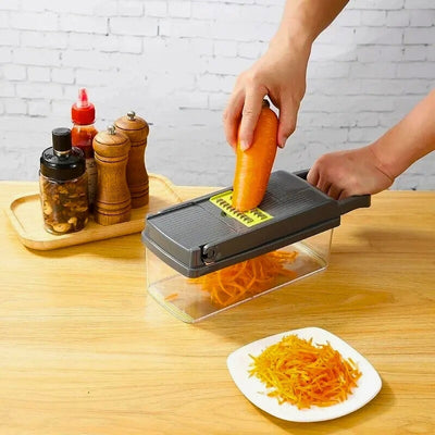 Mandoline cuisine avec réservoir posée sur une table et utilisé par une personne pour râper une carotte, à côté une assiette de carottes râpées.