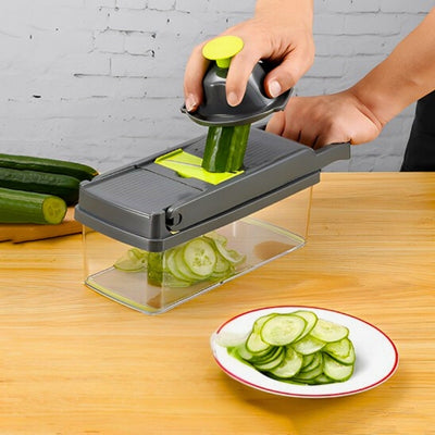 Mandoline cuisine avec réservoir posée sur une table et utilisé par une personne pour couper un concombre, à côté une assiette de concombres coupés en rondelle