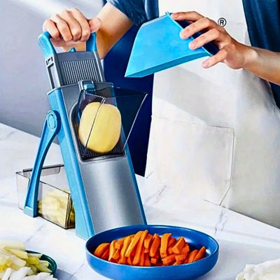 Mandoline cuisine bleue posée sur un plan de travail et utilisée par une personne pour couper une pomme de terre, devant une assiette remplie de carottes coupées en bâtonnet.