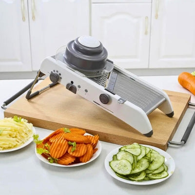 Mandoline cuisine posée sur une table avec des assiettes remplies de légumes coupés posées devant.