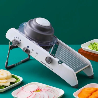Mandoline cuisine posée sur table avec assiette de légumes découpés.