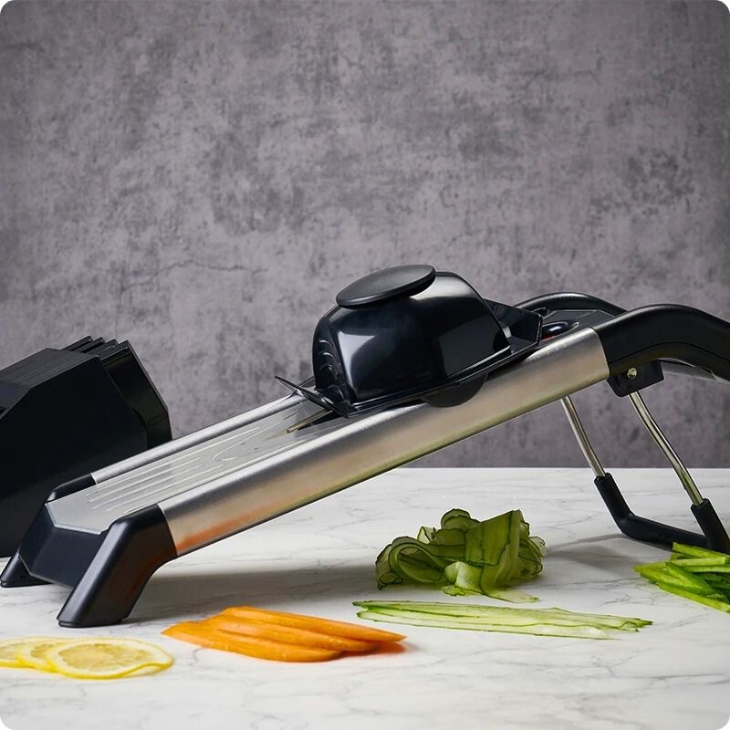 Mandoline japonaise sur table avec légumes coupés proprement à côté.