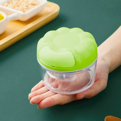 Main qui soutient un mini hachoir vert à côté d'un plateau en bois.